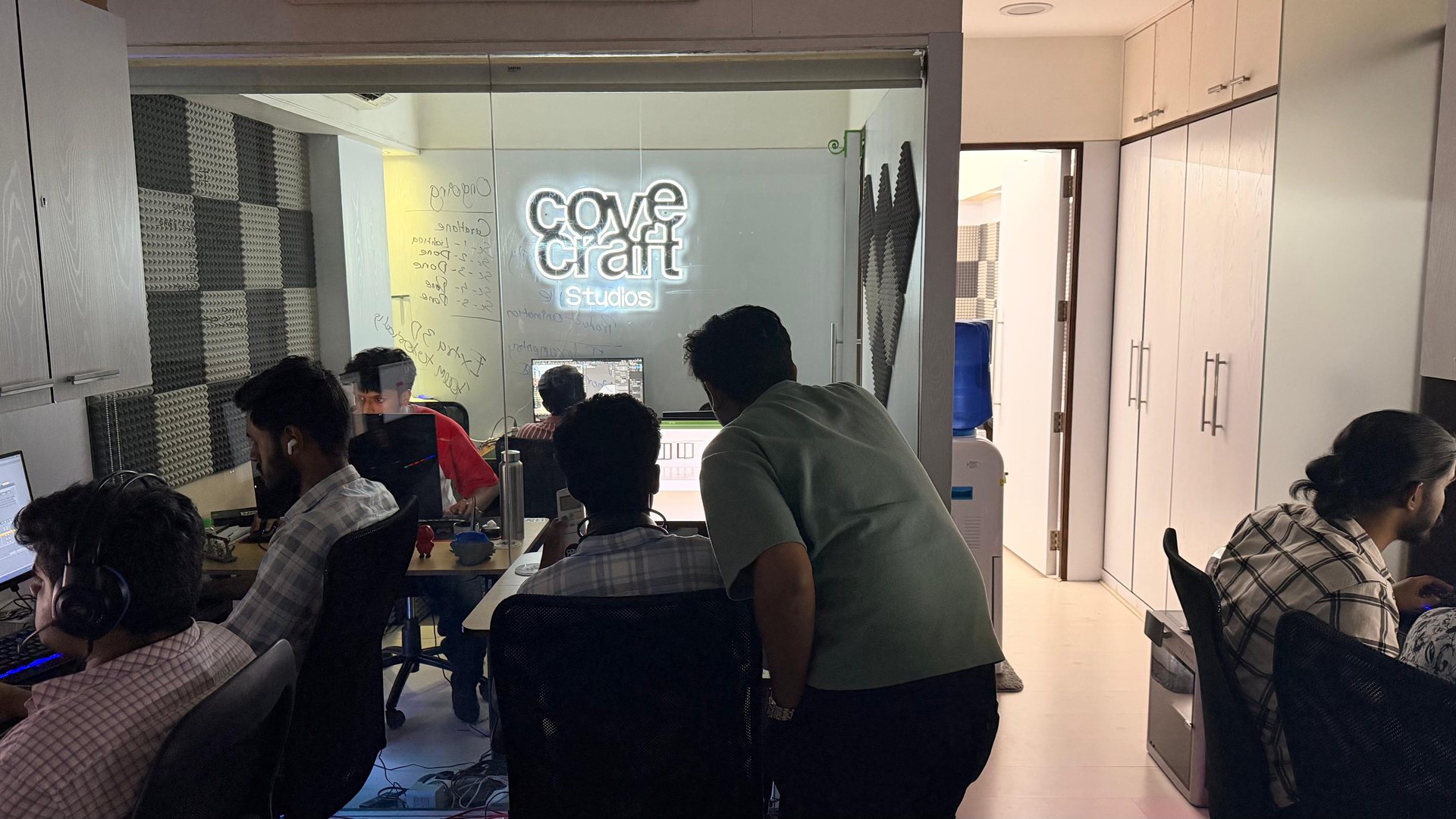 The Cove Craft Studios team working at their desks under the studio’s neon sign